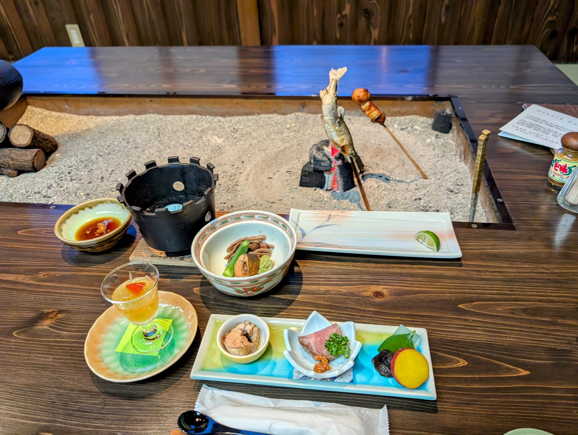 Open fire in the center of the kneeling-height table. Sunken cut-out for your legs to sit normally while staff can kneel next to your table.