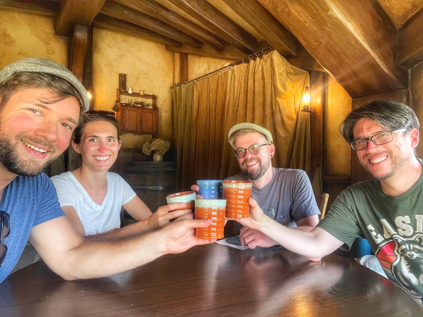Three men and a woman clinking mugs together in the Green Dragon tavern in Hobbiton