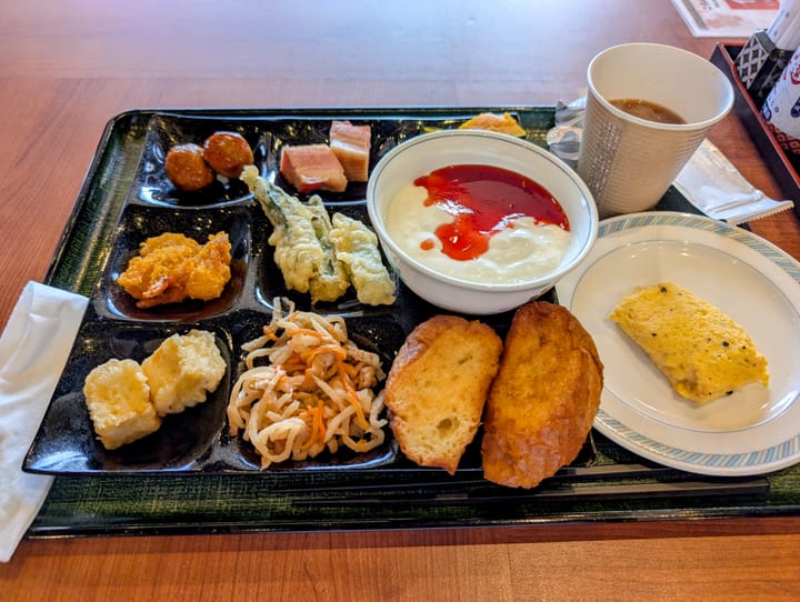 A tray with numerous smaller divets for foods, containing small portions of various Japaneses dishes, and a few Western as well.