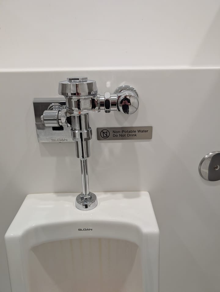 An automatic urinal found in the PDX airport with a sign saying "Non-Potable Water Do Not Drink"